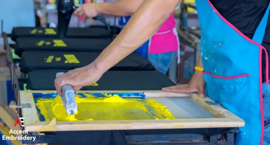 A man in an apron operates a screen printing machine, preparing custom t shirts for printing A man in an apron operates a screen printing machine, preparing custom t shirts for printing